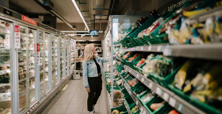 Woman standing in supermarket shopping aisle looking at vegetables