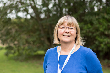 smiling female standing on gard area, with trees and bushes in background