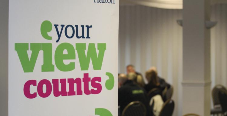 Image of a banner. Text reads, 'Healthwatch Halton, your views count'. blurred image of people sitting at a table in the background