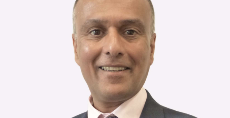  Raj Jain, Chair of NHS Cheshire and Merseyside, smiling at the camera. He is wearing a navy blue suit, light pink shirt, and a purple tie with yellow polka dots, set against a plain light background.