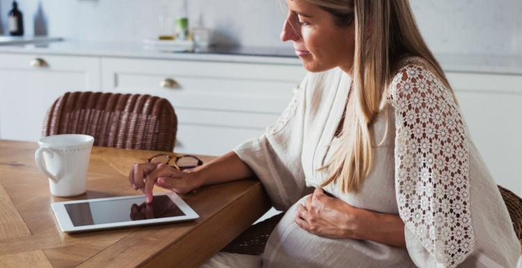 A pregnant woman uses a tablet device at home. 