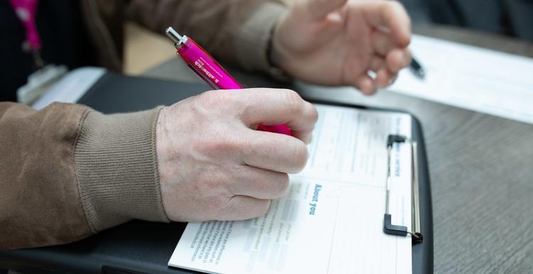 Person writing on a clipboard with a Healthwatch pen. 