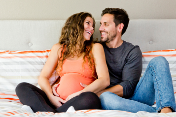 photo of man and pregnant woman sitting on a bed smiling