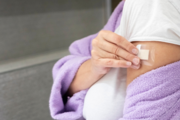 A woman in a purple bath robe places a HRT patch on her arm.
