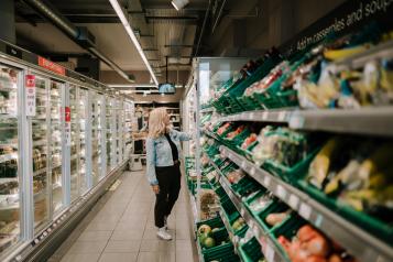 Woman standing in supermarket shopping aisle looking at vegetables