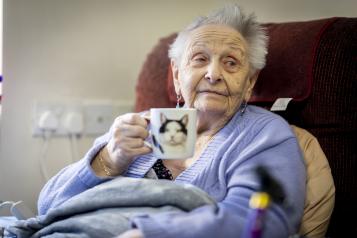 woman relaxing in a chair, holding a cup with an image of a cat on it.