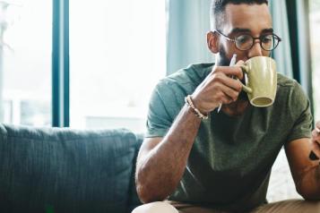 A man uses his mobile phone whilst drinking from a mug. 