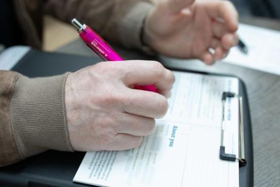 Person writing on a clipboard with a Healthwatch pen. 